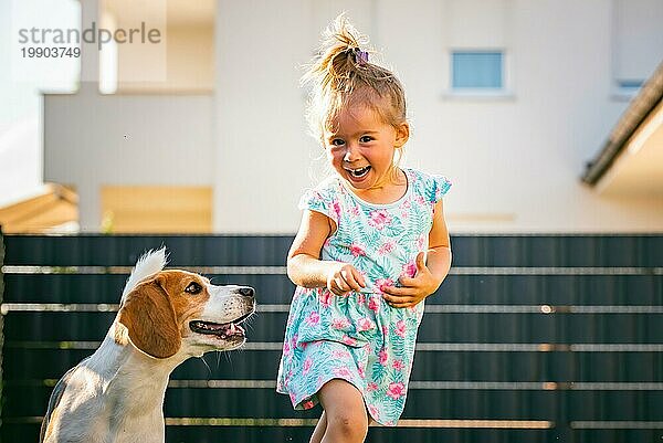 Baby Mädchen läuft mit Beagle Hund im Hinterhof im Sommer Tag. Haustier mit Kindern Konzept. Hund jagt 23 Jahre alt  läuft nach Leckerbissen