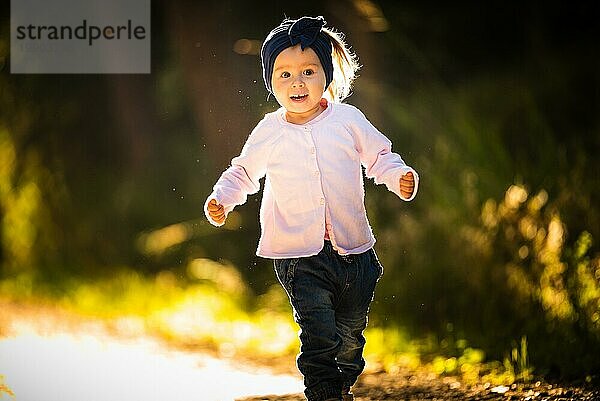 2 Jahre altes Baby Mädchen läuft im Wald in Richtung Kamera. mit glücklichen Ausdruck auf ihrem Gesicht. Baby in der Natur Konzept