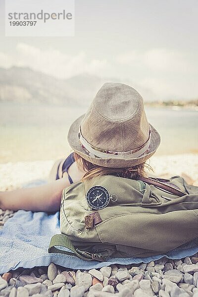 Weltreise: Kompass im Vordergrund  Mädchen am Strand liegend im unscharfen Hintergrund