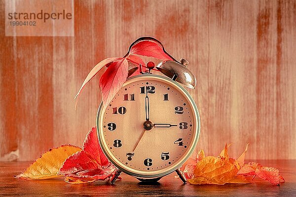 Daylight Savings Time Konzept  Herbst zurück in den Herbst  getönten Bild. Ein Vintagewecker mit Herbstblättern auf einem rustikalen Holzhintergrund