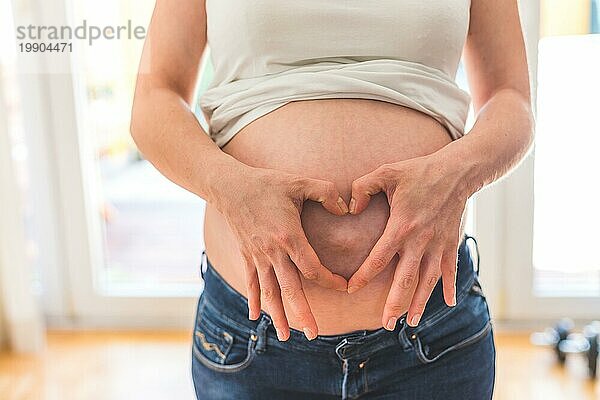 Glückliche kaukasische schwangere Mutter  die ihren nackten Bauch berührt  Blue Jeans  Nahaufnahme