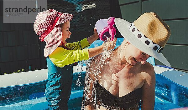 Baby gießt Wasser auf Mutter im Babyschwimmbad. Kinder Spaß im Wasser Thema