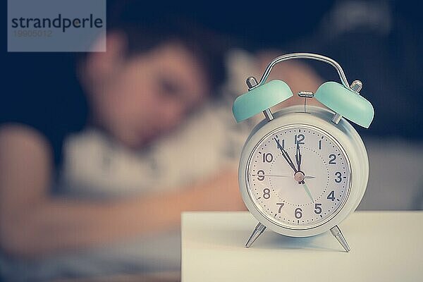 Weißer Wecker auf dem Nachttisch. Junger Mann schläft im Hintergrund