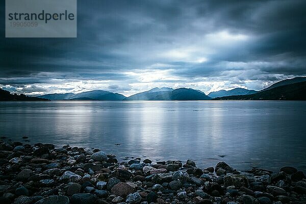 Schöne mystische Landschaft Seelandschaft in Schottland mit bewölktem Himmel und Sonnenstrahlen