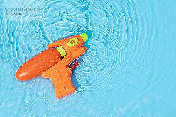 Wasserpistole Spielzeug auf blaün Wasseroberfläche mit gekräuselten Wellen. Spaß  Freizeit Sommerzeit Hintergrund. Raum kopieren