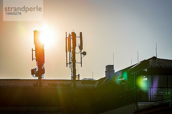 Silhouette eines Fernmelde oder Mobilfunkmastes auf dem Dach eines Gebäudes  Abendsonne