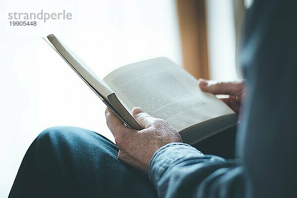 Ausgeschnittenes Bild eines älteren Mannes  der zu Hause ein Buch liest