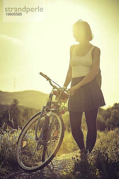 Junge Frau mit Fahrrad genießt die Abendsonne