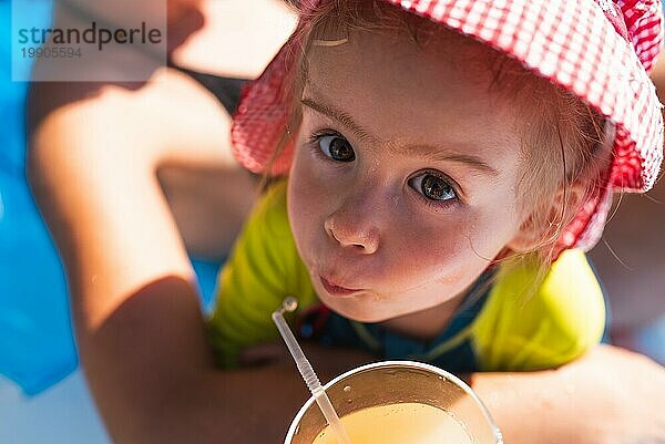 Niedliches kleines Mädchen trinkt draußen Saft mit einem Strohhalm. Baby im Sommer Thema