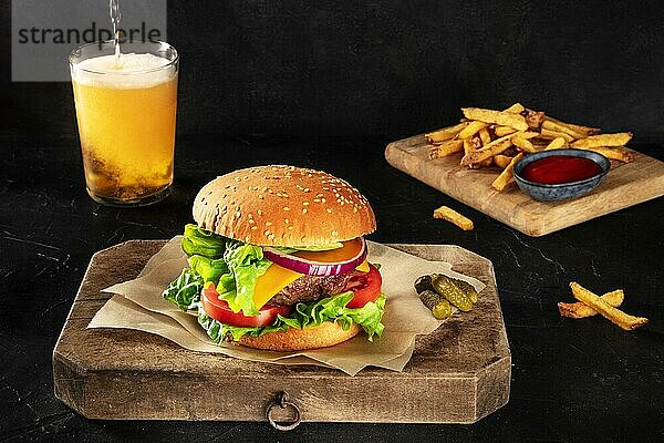 Burger mit Pommes frites und Bier. Hamburger mit Rindfleisch  Käse  Zwiebel  Tomate und grünem Salat  auf dunklem Hintergrund mit Leerzeichen. Selektiver Fokus