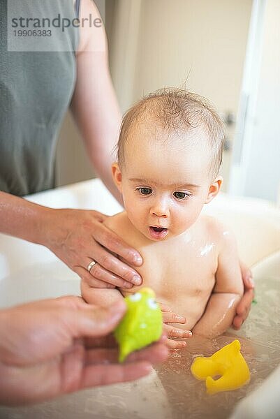 6 Monate Baby baden Konzept. Baby in der Badewanne konzentriert sich auf ein Spielzeug. Baby Entwicklung