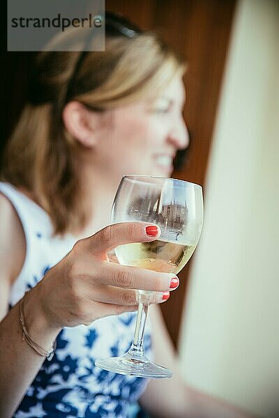 Schönes junges Mädchen mit blondem Haar hält ein Glas Wein und lächelt  Ferien