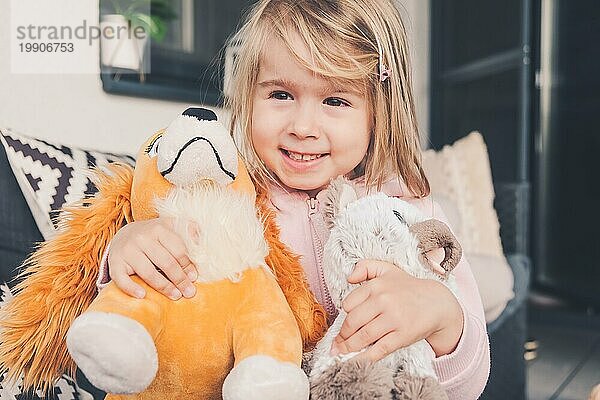 Kleines Mädchen lächelnd und umarmt zwei Plüschtiere Hund und Katze. Kindheit Konzept 3 4 Jahre alt