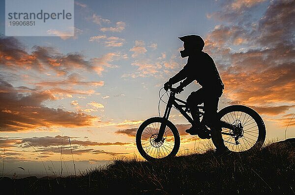 Silhouette eines Radfahrers auf einem Sportfahrrad vor einem Hintergrund von Sonnenuntergangswolken hoch in den Bergen