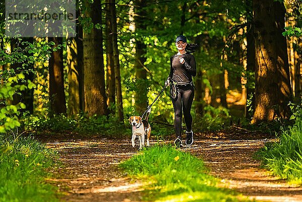 Mädchen läuft mit einem Hund (Beagle) an der Leine im Frühling  sonniger Tag im Wald. Kopieren Raum in der Natur