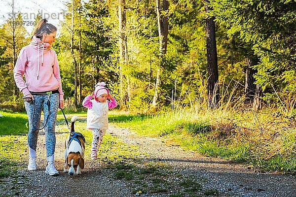 Junge Mutter mit Kind und Hund beim gemeinsamen Spaziergang auf einem Feldweg im Wald. Fröhliche 2 Jahre alt im Freien mit ihrem Haustier