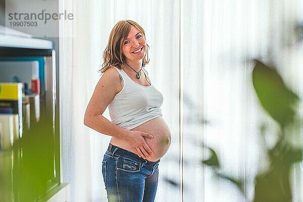 Glückliche kaukasische schwangere Mutter  die ihren nackten Bauch berührt  Blue Jeans  Nahaufnahme