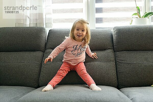 2 Jahre altes Baby Mädchen auf Couch in hellem Interieur. Aktives Kind Konzept