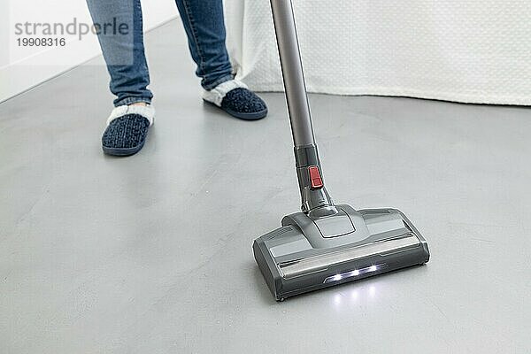 Frau beim Reinigen mit einem kabellosen Staubsauger in einem modernen Schlafzimmer. Raum kopieren