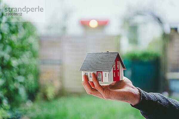 Neues Haus und Hauskonzept: Rotes Hausmodell im Freien in männlicher Hand