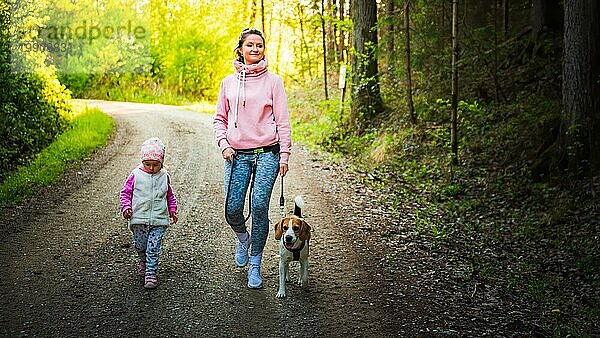 Junge Mutter mit Kind und Hund beim gemeinsamen Spaziergang auf einem Feldweg im Wald. Fröhliche 2 Jahre alt im Freien mit ihrem Haustier