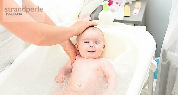 Bezauberndes kleines Mädchen in der Badewanne mit Mutter. Sie schaut mit großen braunen Augen auf und lächelt. Leerzeichen kopieren