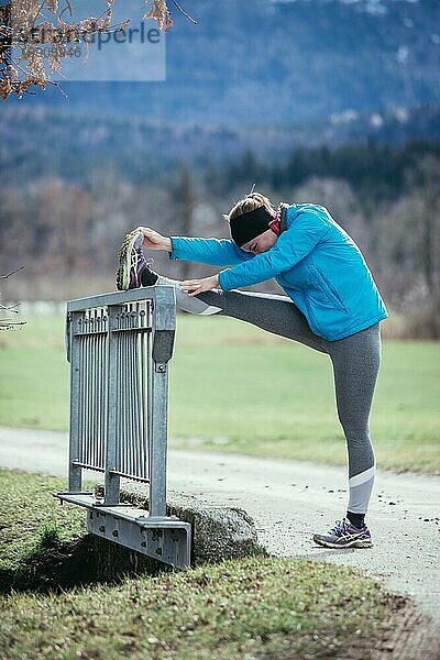 Junge Frau beugt und streckt sich  bevor sie zum Laufen geht