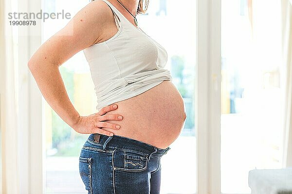 Glückliche kaukasische schwangere Mutter  die ihren nackten Bauch berührt  Blue Jeans  Nahaufnahme