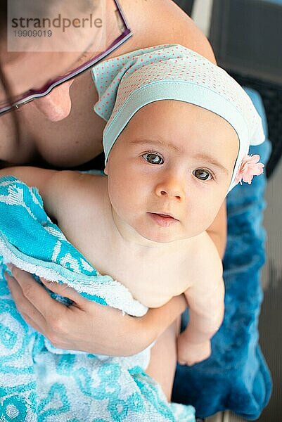 Mutter hält kleines Mädchen auf dem Schoß  bedeckt mit Handtuch nach dem Schwimmen. Sommeraktivitäten