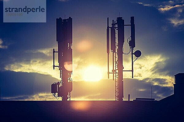 Silhouette eines Fernmelde oder Mobilfunkmastes auf dem Dach eines Gebäudes  Abendsonne