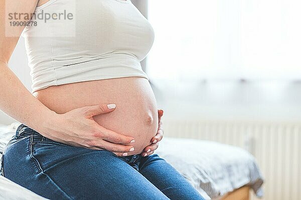 Kaukasische schwangere Mutter  die ihren nackten Bauch berührt  Blue Jeans  Nahaufnahme