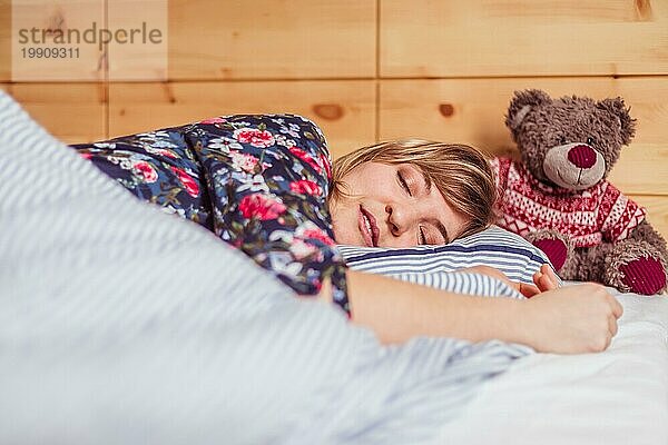 Junge Frau schläft friedlich mit ihrem Teddybär in ihrem Schlafzimmer