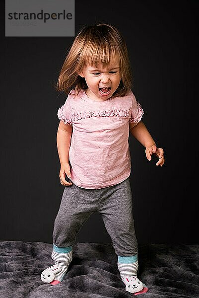 2 Jahre altes Kind mitangry Ausdruck alle vier vor weißem Hintergrund. Cutout Foto für Konzept der Entwicklung von Emotionen. Mädchen in rosa Hemd