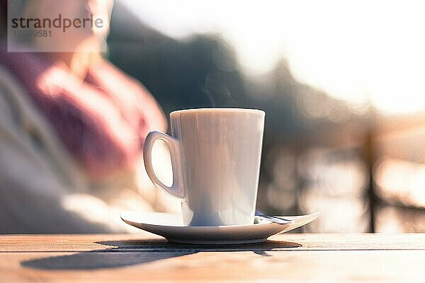 Tasse Kaffee  mit einer Frau im unscharfen Hintergrund. Draußen