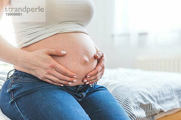 Kaukasische schwangere Mutter  die ihren nackten Bauch berührt  Blue Jeans  Nahaufnahme