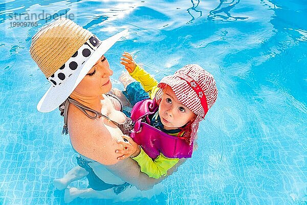 23 Jahre altes Kind mit Mutter im Schwimmbad lernen zu schwimmen. Baby im Schwimmen Westen und roten Hut.Sommer zu Hause Konzept. Oben schießen