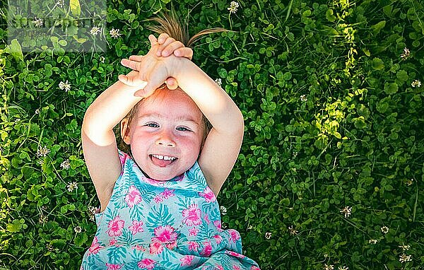 Schönes kleines Mädchen liegt im Gras und lacht und schaut nach oben. 23 Jahre altes Kind in der Natur an einem sonnigen Sommertag