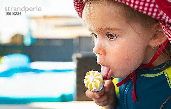 Portrait kleines Kind mit großen Augen leckt Eis im Sommer. 2 Jahre altes Baby Mädchen. Kinder essen Süßigkeiten