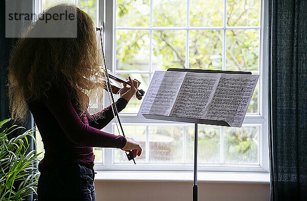 Mädchen übt zu Hause vor dem Fenster Geige