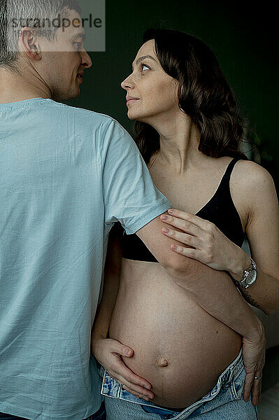 Loving man and pregnant woman looking at each other against dark background