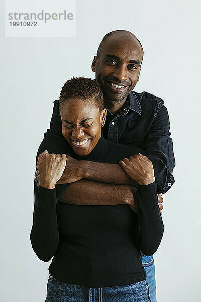 Smiling man with arms around happy woman against white background