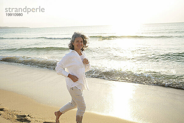 Lächelnde reife Frau läuft am Strand