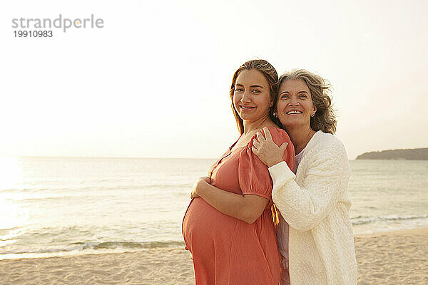 Glückliche schwangere Frau steht mit Mutter am Strand