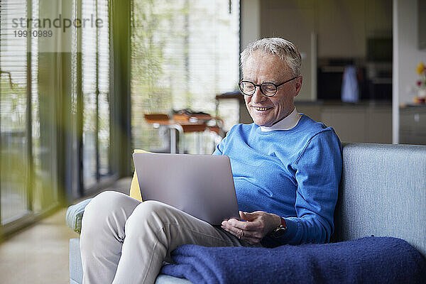 Senior man sitting on couch at home using tablet PC
