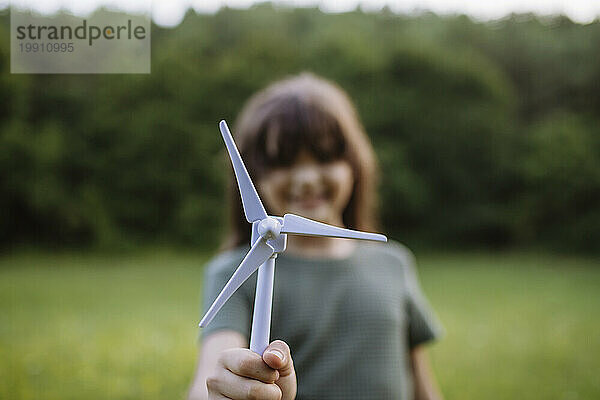 Mädchen steht in der Natur und hält ein Modell einer Windkraftanlage
