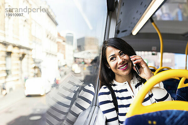 Lächelnde Frau  die im Bus mit dem Handy telefoniert