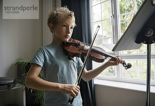 Grundschuljunge spielt Geige am Fenster zu Hause