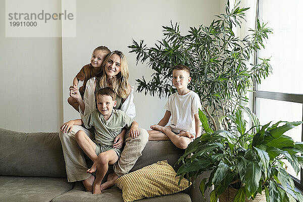 Lächelnde blonde Mutter und Kinder sitzen zu Hause auf dem Sofa