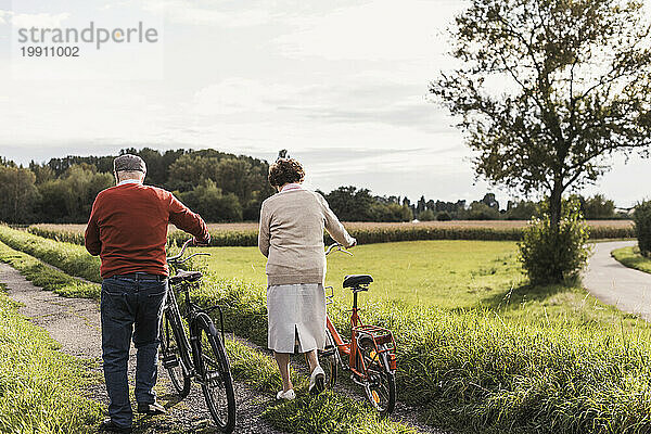 Älteres Paar mit Fahrrädern läuft auf Fußweg im Feld