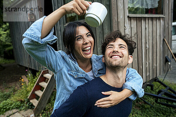 Glücklicher Mann und Frau halten Kaffeetasse in der Nähe einer Holzhütte
